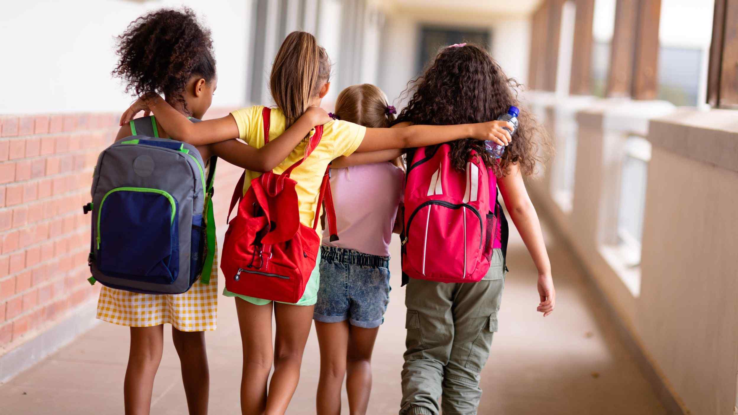 School friends with backpacks holding each other around the shoulders