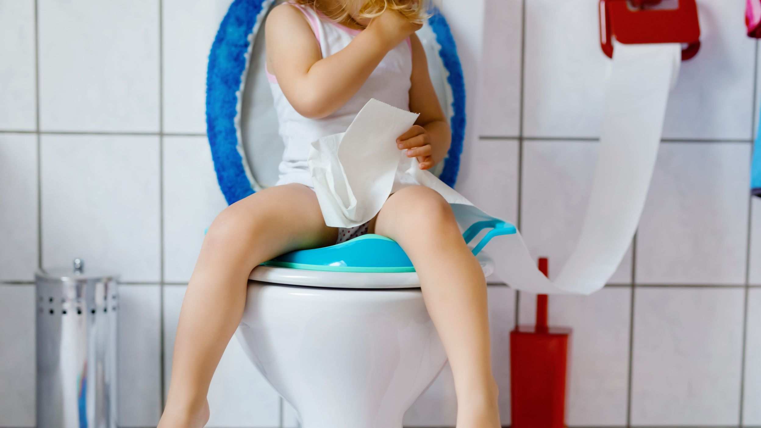 A girl sitting on the toilet with toilet paper in her hand
