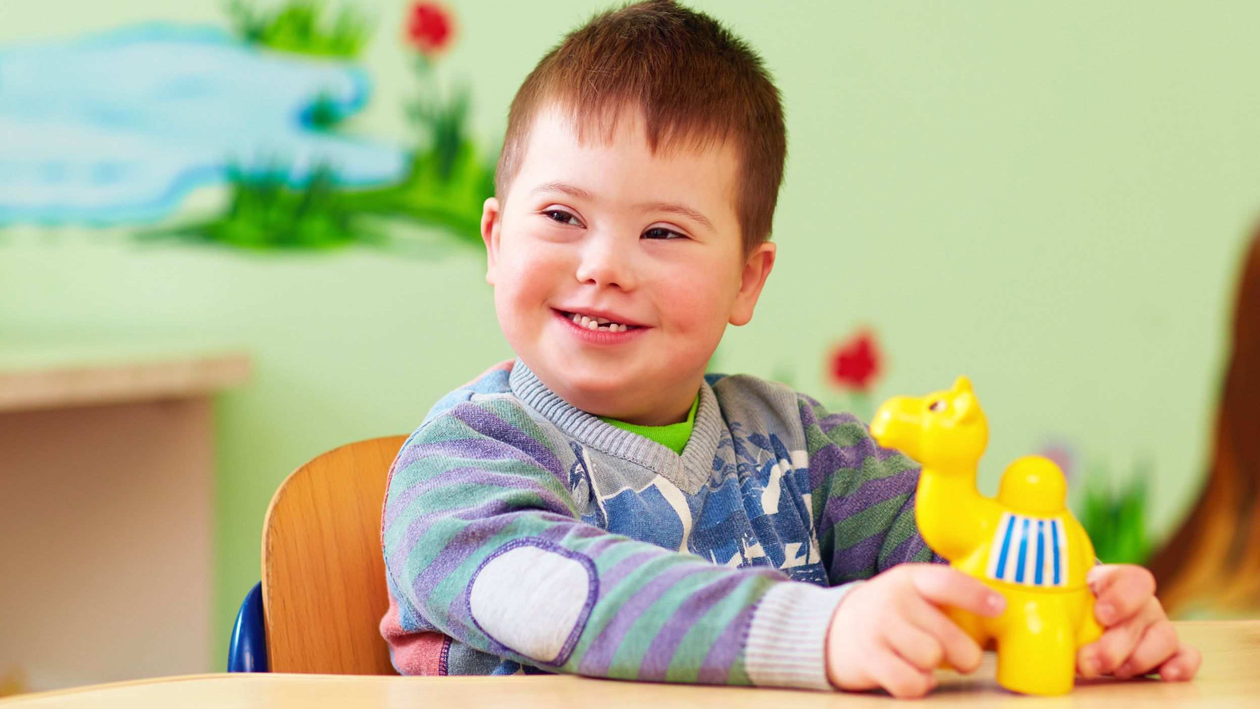 A smiling boy sitting at a table with a toy camel