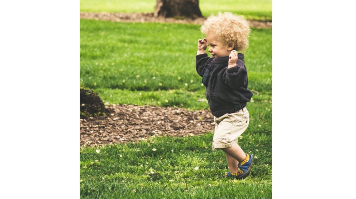 Smiling toddler with blond curly hair running outdoors

