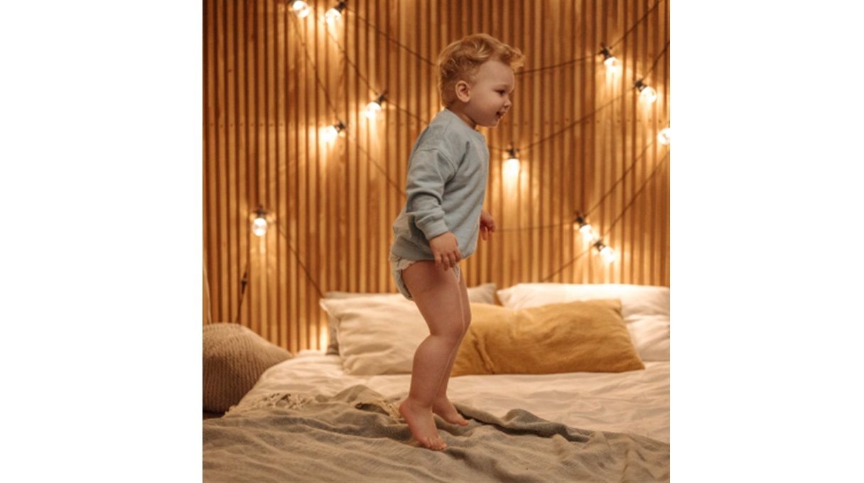 Smiling toddler wearing a nappy while jumping on his bed
