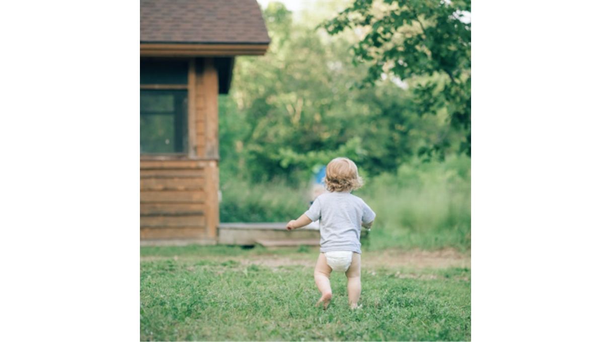 Smiling toddler wearing a nappy while running outdoors

