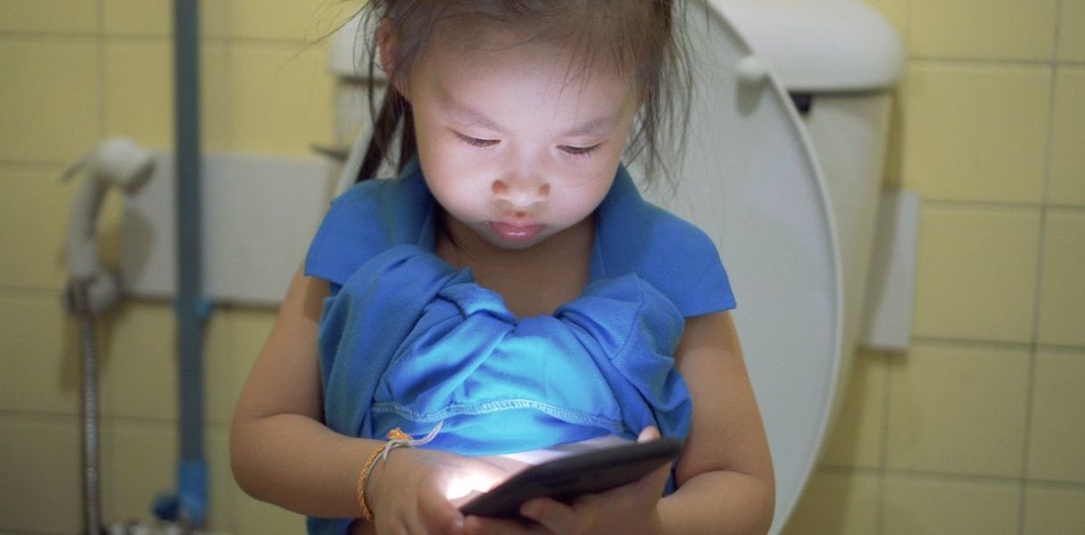A girl sitting on the toilet while holding a mobile device