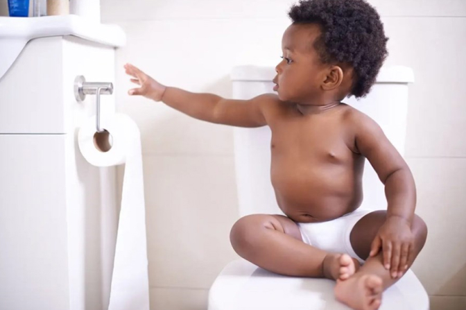 Child sitting on a toilet and reaching out to toilet paper