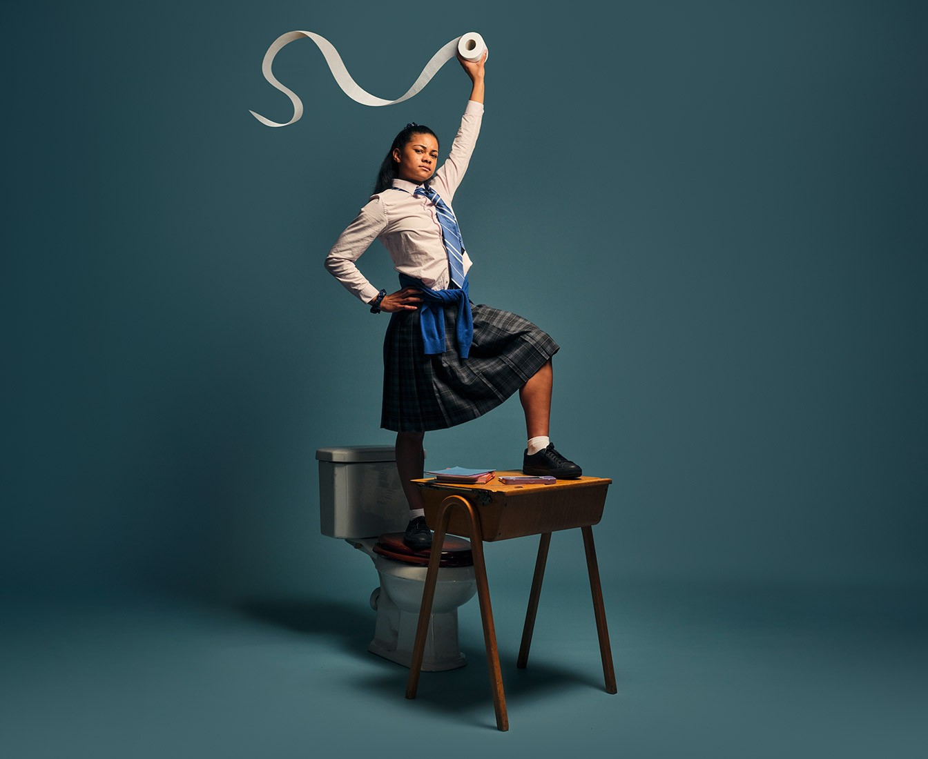 A confident school boy sitting on a toilet with his feet propped up on school books
